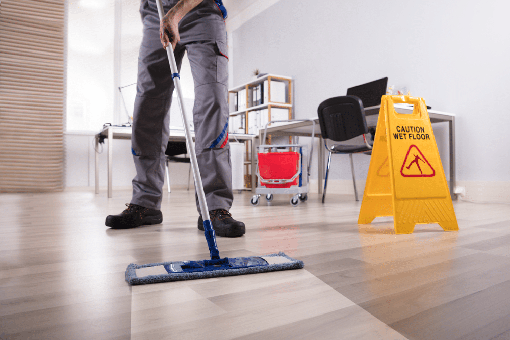 Male Janitor Cleaning Floor With Caution Wet Floor Sign