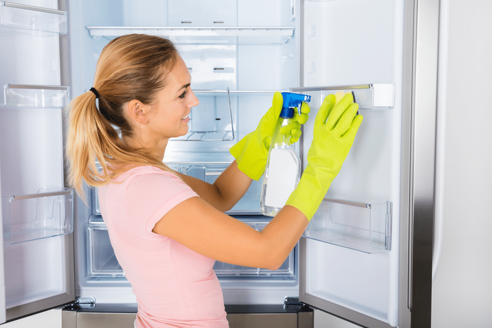 Woman Cleaning The Empty Refrigerator Door With Spray Bottle And Sponge